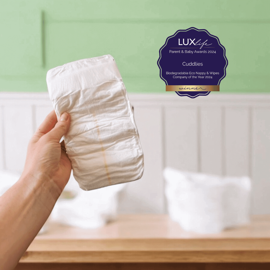 Hand holding a Cuddlies eco bamboo nappy with award badge – recognised for biodegradable nappy care