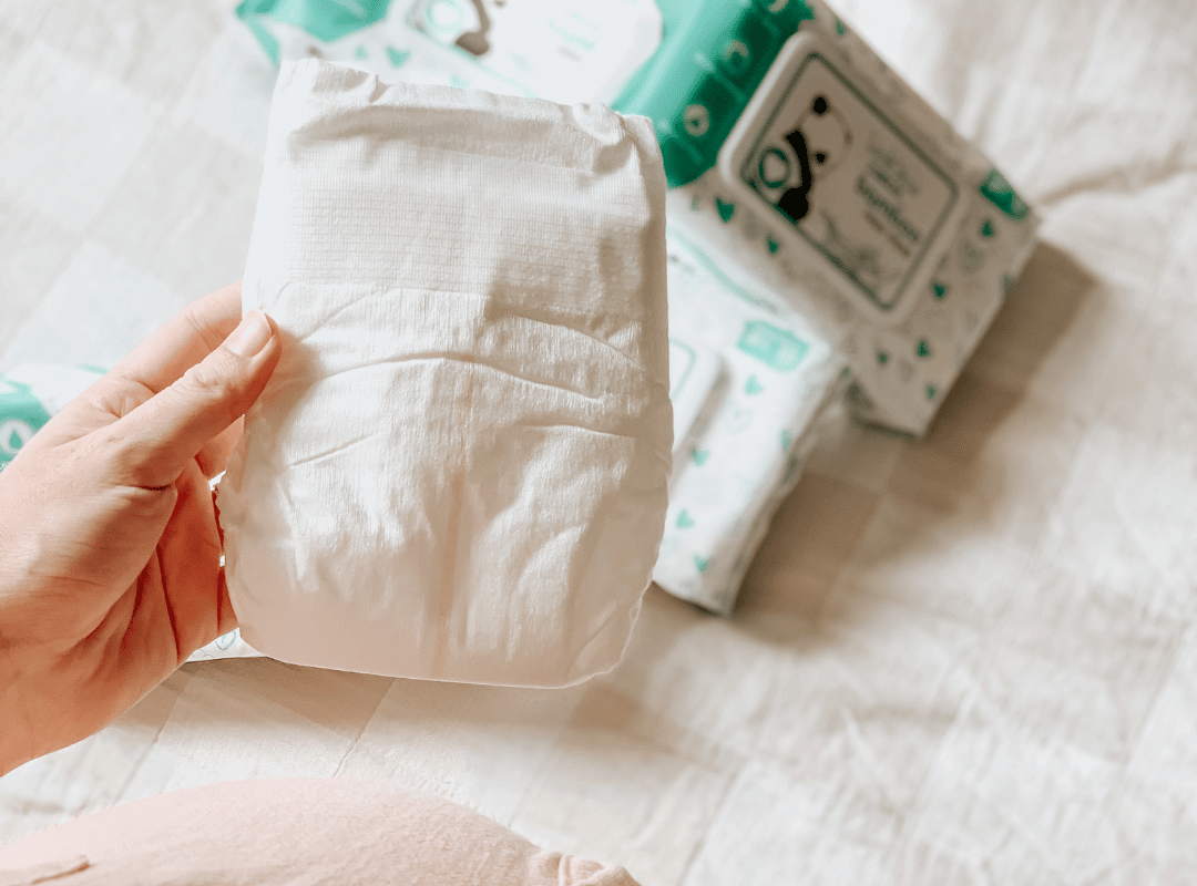 A hand holding a nappy or diaper with wipes in the background