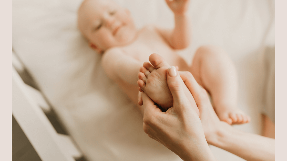 A happy baby wearing eco nappy lying down with feet up getting a massage