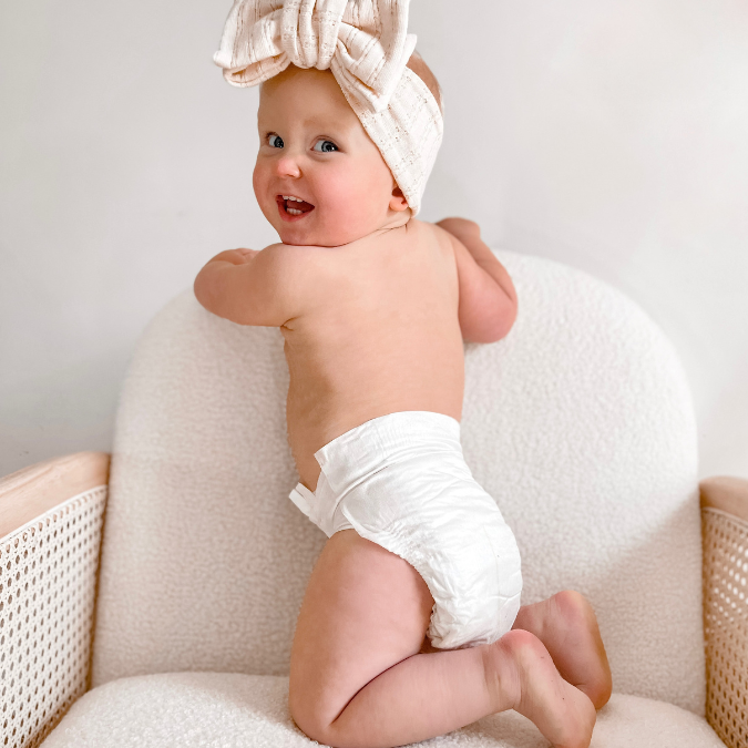 Baby kneeling wearing Cuddlies nappies smiling