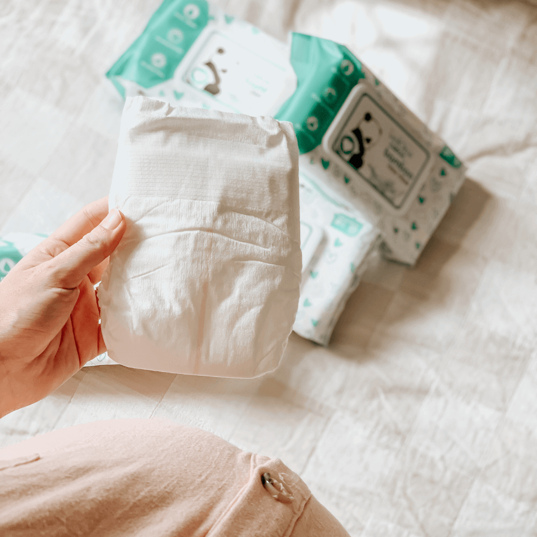 Pregnant mum holding a Cuddlies Eco Nappy and Baby Wipes in background